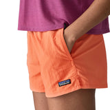 Woman wearing Patagonia's quick drying women's barely baggies shorts in bright orange with hand in side pocket. Shorts have a loose fit