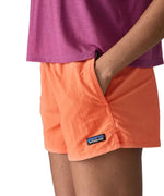 Woman wearing Patagonia's quick drying women's barely baggies shorts in bright orange with hand in side pocket. Shorts have a loose fit
