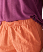 Woman wearing Patagonia's quick drying women's barely baggies shorts in bright orange showing elasticated waist band