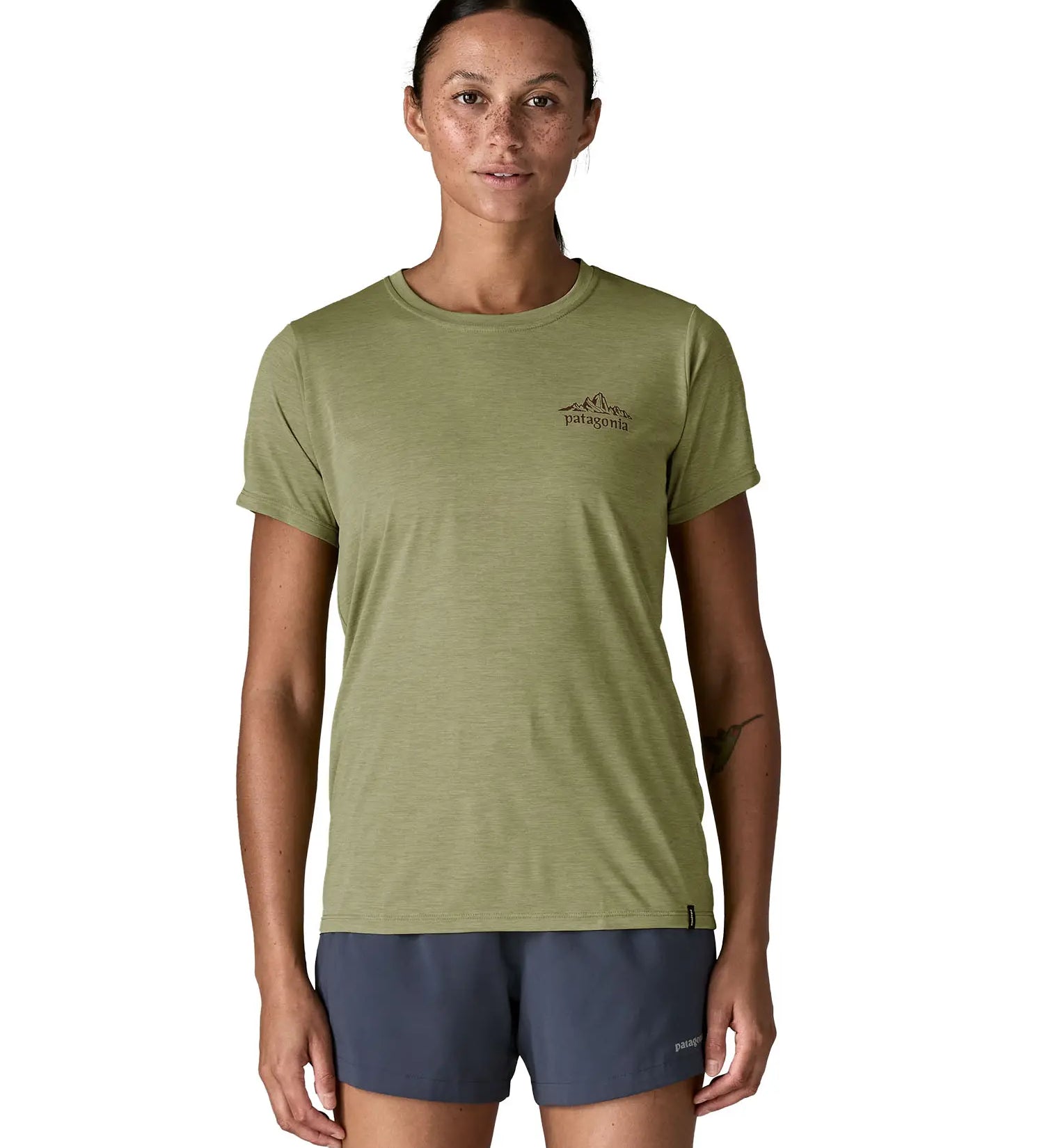 Woman wearing Patagonia women's capilene cool daily short sleeve t-shirt in green showing mountain graphic on upper chest. T-shirt has a relaxed fit