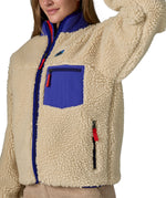An image of a women wearing the Patagonia women's classic retro-x jacket in a dark natural colour way available at Babipur showing the royal blue trim detail