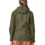 The back of the Patagonia Women's Torrentshell 3L Rain Jacket - Pine Needle Green. The image shows a person wearing the jacket to show the fit of the coat from the back and the hood