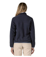 Back of a woman wearing Patagonia's synchilla snap t fleece in dark blue. Fleece has a relaxed fit and sits around the hips