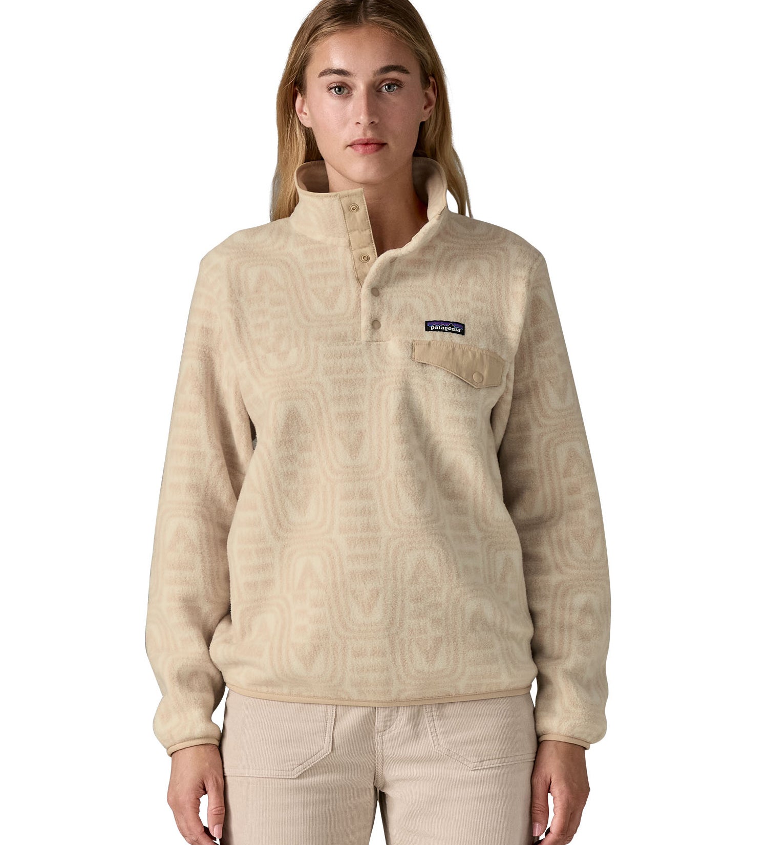 A woman wearing the Patagonia women's synchilla jacket in flow dyno white available at Babipur. A light cream flowing patterned fleece type jacket. Features the logo patch stitched on the left chest pocket, popper fasteners and a chest pocket. 