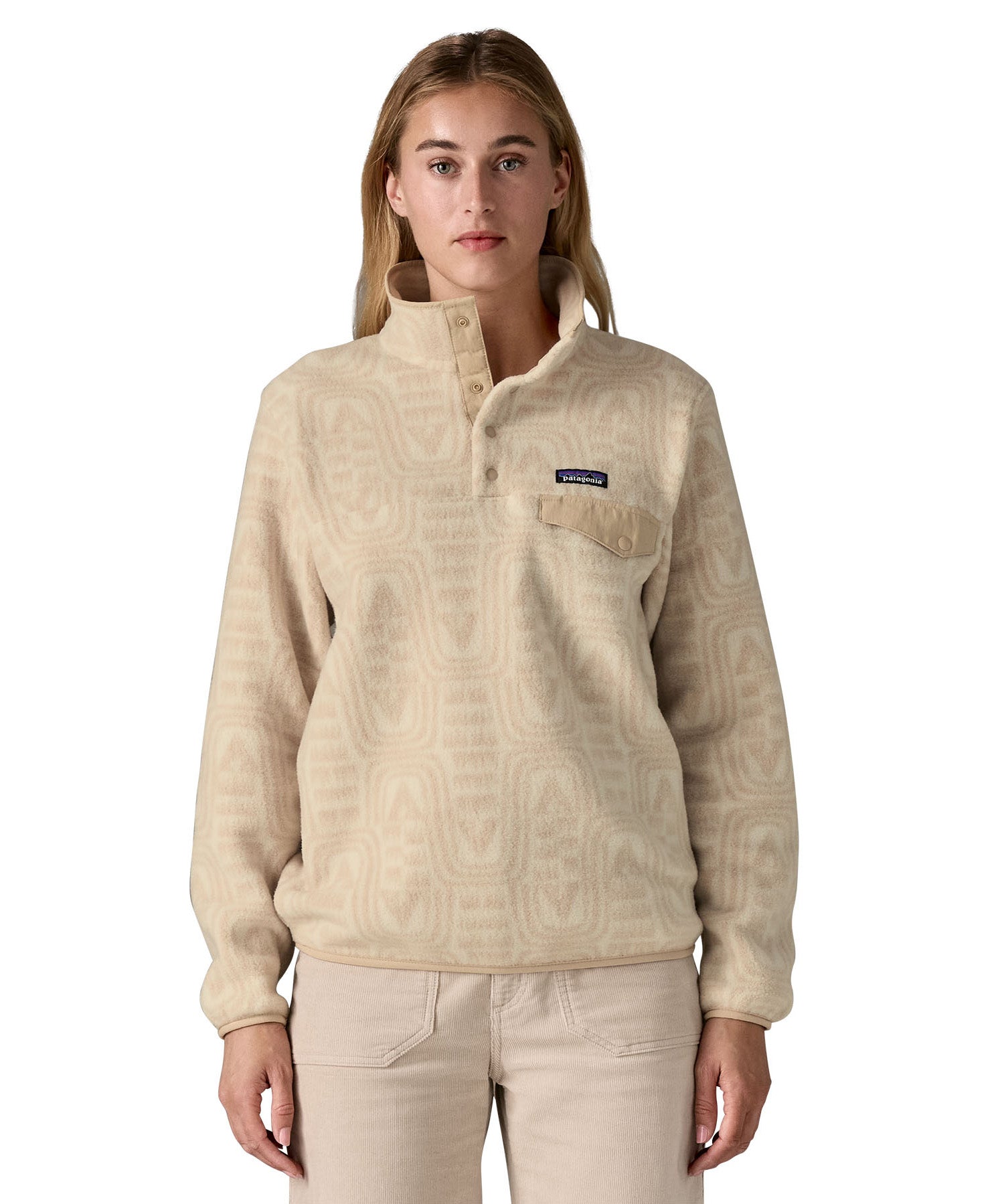 A woman wearing the Patagonia women's synchilla jacket in flow dyno white available at Babipur. A light cream flowing patterned fleece type jacket. Features the logo patch stitched on the left chest pocket, popper fasteners and a chest pocket. 