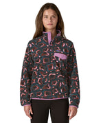 A woman wearing the Patagonia women's synchilla jacket in soft spirea dried vanilla available at Babipur. A green, brown and pink patterned fleece type jacket. Features the logo patch stitched on the left chest pocket, popper fasteners and a chest pocket. 