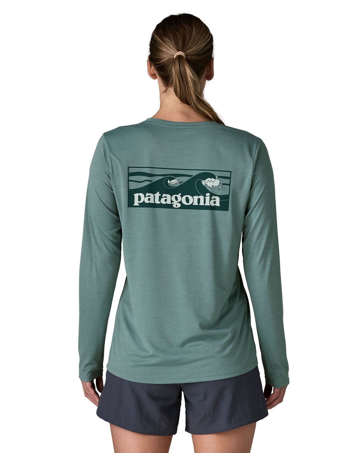 Woman wearing Patagonia's women's long sleeve capilene cool t-shirt in sage blue with wave logo graphic on upper back