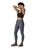 A female standing in front of a white background wearing a sports vest and the Patagonia women's activewear tights in dark blue with side pockets