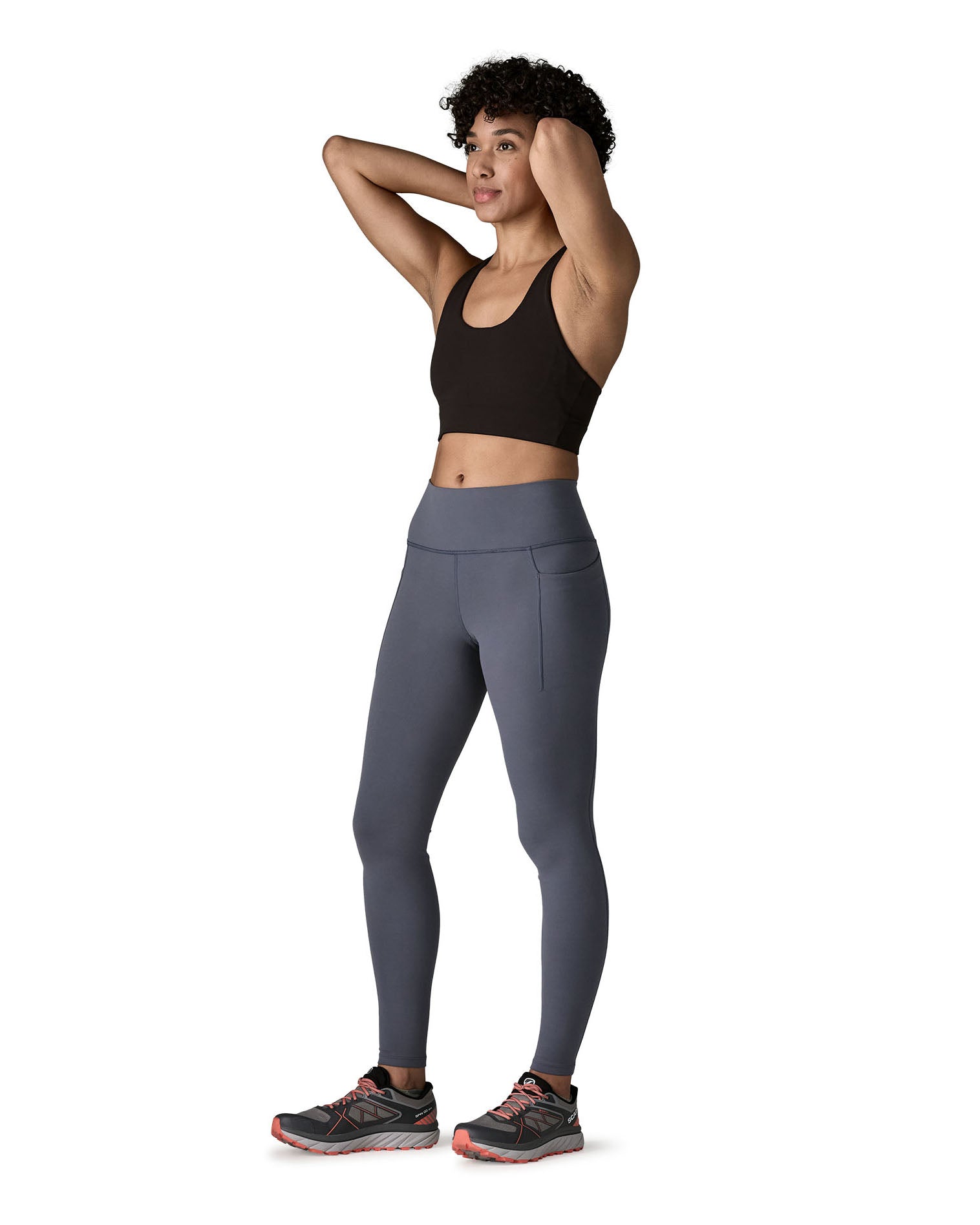 A female standing in front of a white background wearing a sports vest and the Patagonia women's activewear tights in dark blue with side pockets