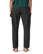 The back of the female standing in front of a white background wearing sandals and the Patagonia women's lightweight cargo trousers in black showing the leg length of the trousers