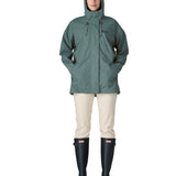 Front of woman wearing Patagonia outdoor everyday rain jacket in blue sage with the hood up. Coat has a straight hemline falls below the bum