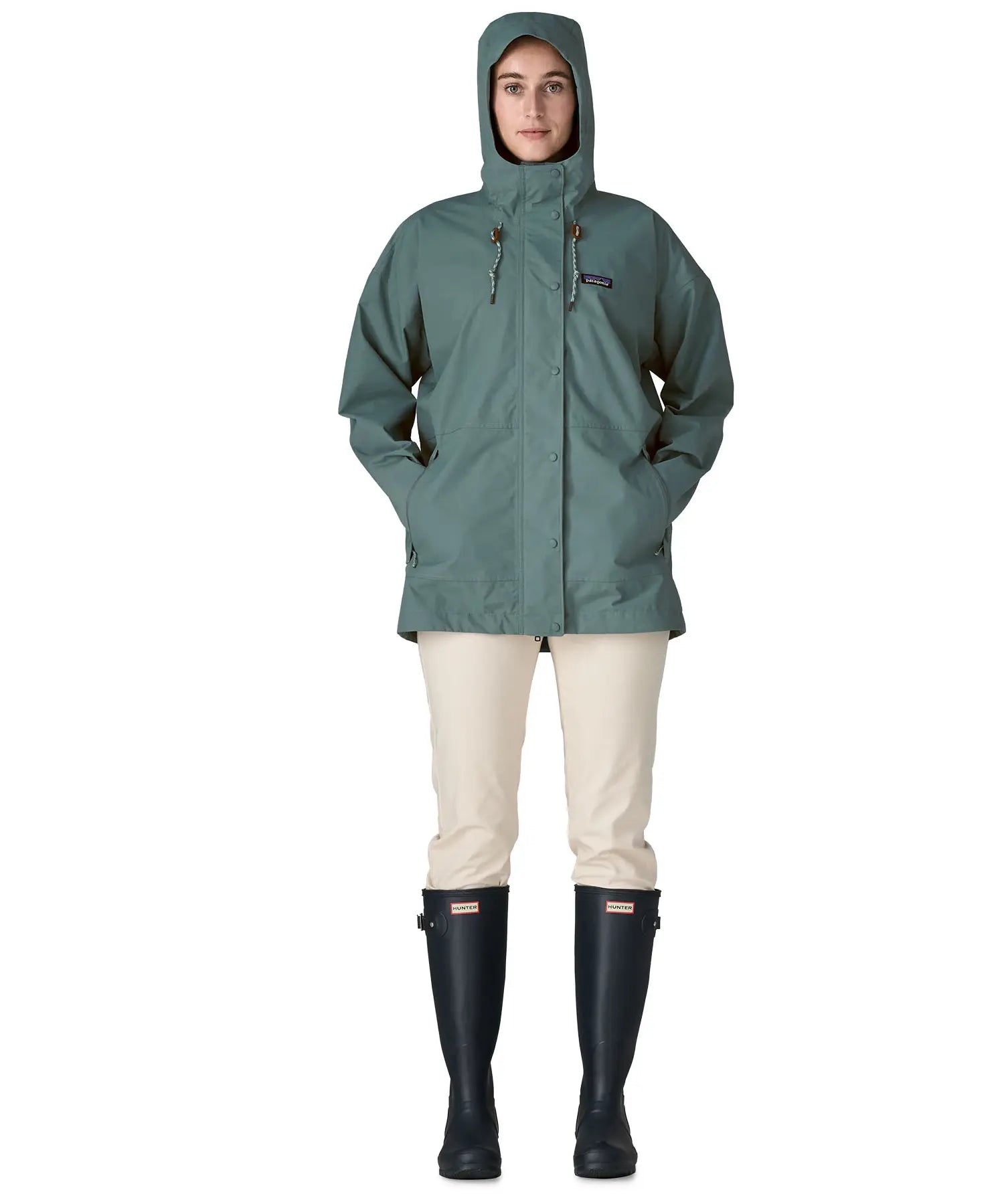 Front of woman wearing Patagonia outdoor everyday rain jacket in blue sage with the hood up. Coat has a straight hemline falls below the bum