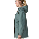 Side of woman wearing Patagonia outdoor everyday rain jacket in blue sage. Coat has a straight hemline falls below the bum