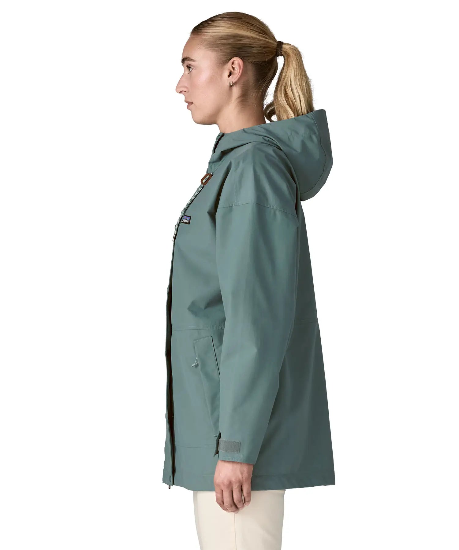 Side of woman wearing Patagonia outdoor everyday rain jacket in blue sage. Coat has a straight hemline falls below the bum