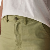 A close up of the female wearing a white and the Patagonia women's canvas trousers in light green colour showing the button fastener detail
