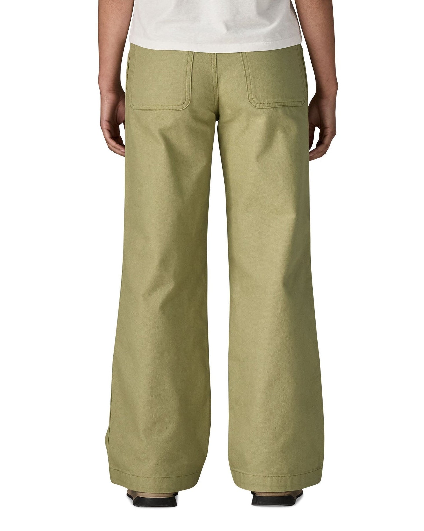 A close up of the back of the female standing in front of a white background wearing a white t-shirt and the Patagonia women's canvas trousers with a wide leg in light green colour showing the leg length and back pocket
