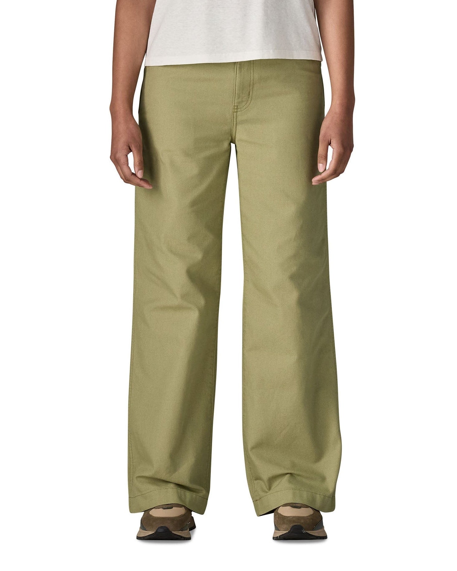 A close up of the female standing in front of a white background wearing a white t-shirt brown trainers and the Patagonia women's canvas trousers with a wide leg in light green colour showing the leg length