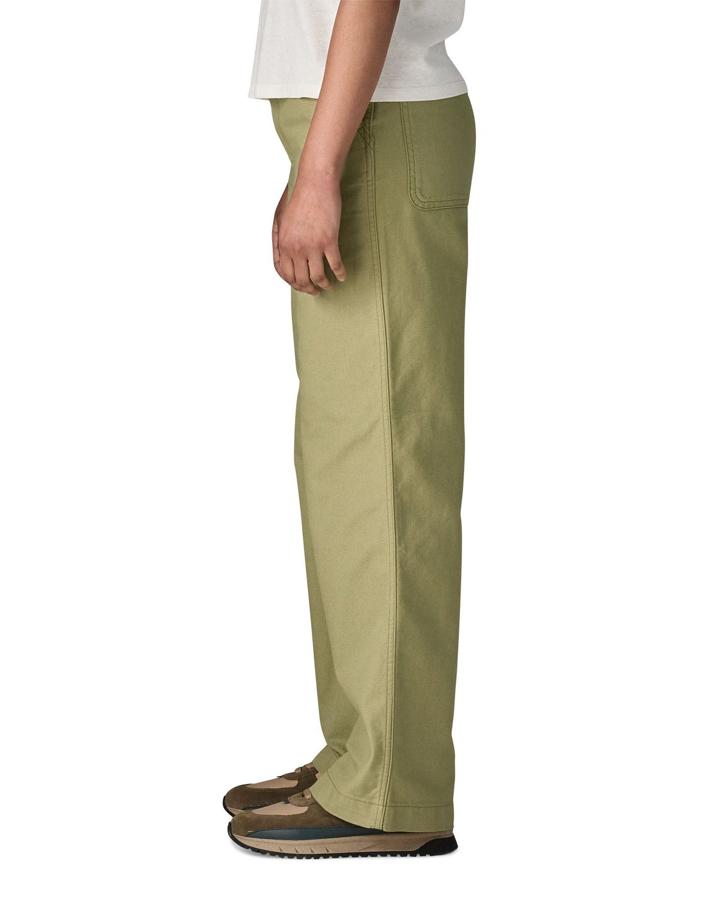 The side of the female standing in front of a white background wearing a white t-shirt brown trainers and the Patagonia women's canvas trousers with a wide leg in light green colour showing the leg length