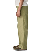 The side of the female standing in front of a white background wearing a white t-shirt brown trainers and the Patagonia women's canvas trousers with a wide leg in light green colour showing the leg length