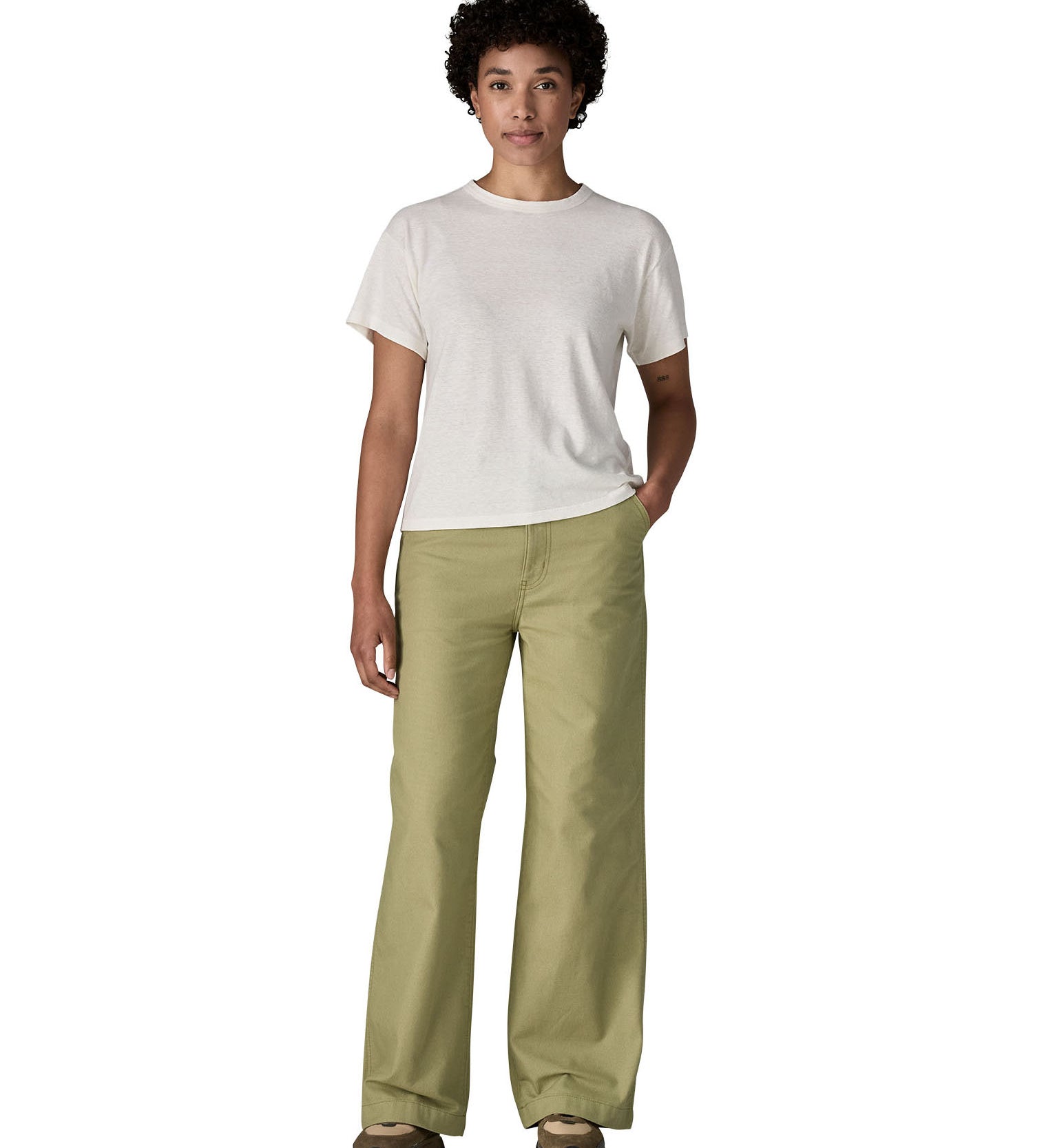 Female standing in front of a white background wearing a white t-shirt brown trainers and the Patagonia women's canvas trousers with a wide leg in light green colour