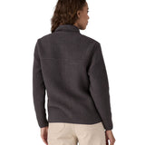 The back of a female in front of a white background wearing cream trousers and a Patagonia thick black fleece jacket with a turned up collar