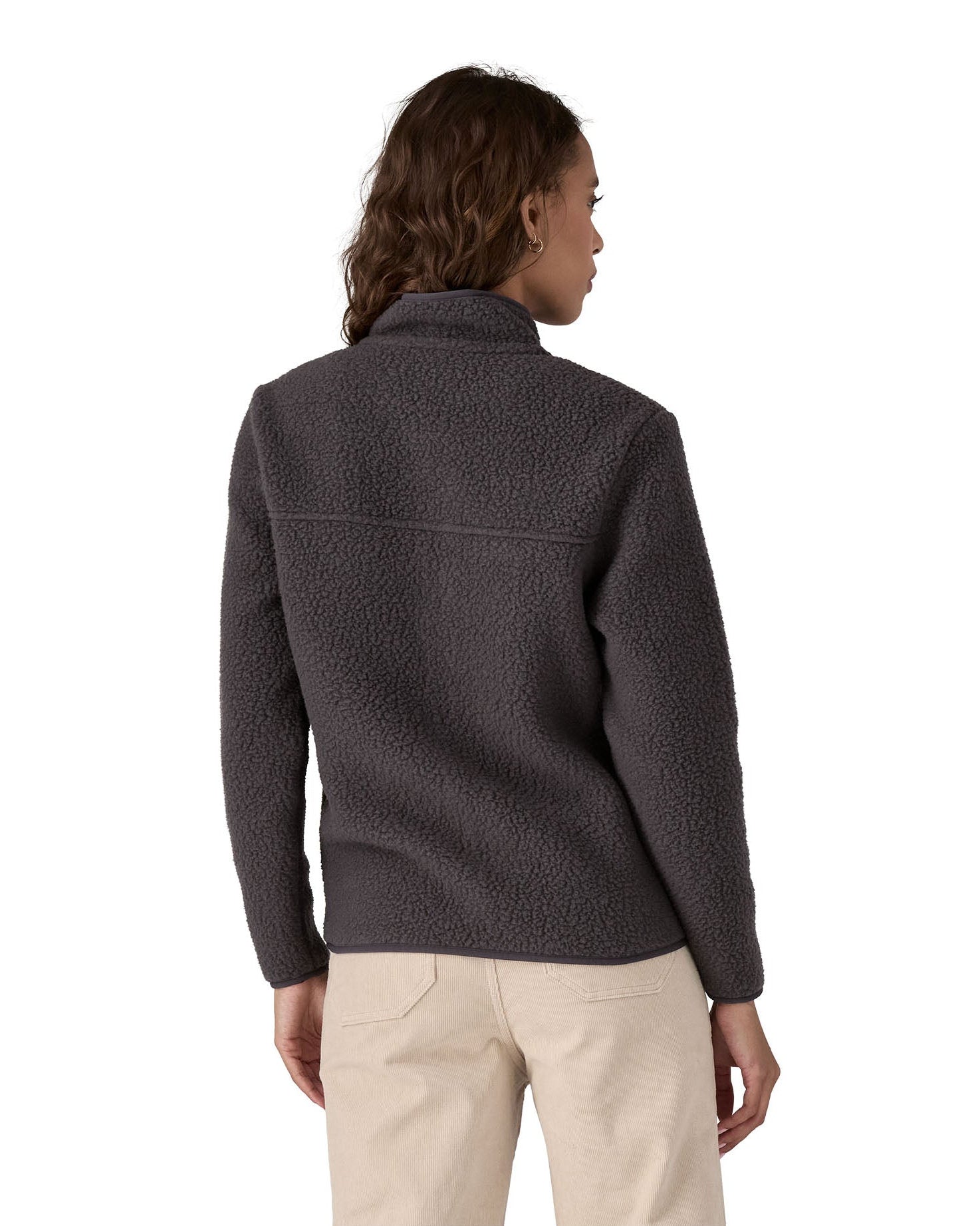 The back of a female in front of a white background wearing cream trousers and a Patagonia thick black fleece jacket with a turned up collar