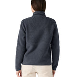 Back of the female standing in front of a white background wearing white trousers and the Patagonia women's thick fleece jacket in dark blue with the collar turned up