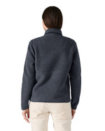 Back of the female standing in front of a white background wearing white trousers and the Patagonia women's thick fleece jacket in dark blue with the collar turned up