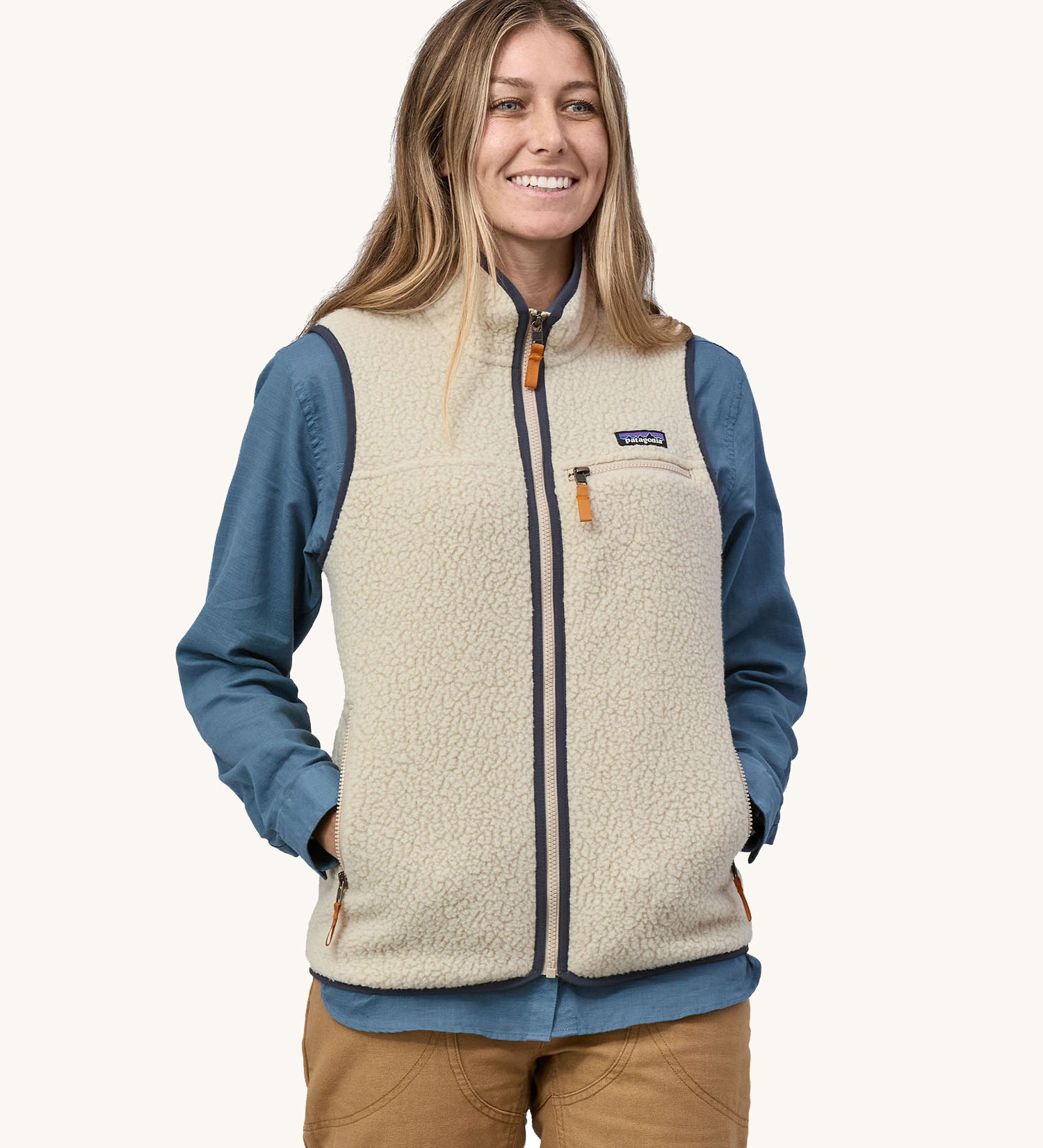 A model wearing the Patagonia women's retro pile fleece vest in pelican. A light cream coloured gilet with a dark blue trim. This gilet features a full length zip, chest and side pockets