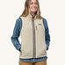 A model wearing the Patagonia women's retro pile fleece vest in pelican. A light cream coloured gilet with a dark blue trim. This gilet features a full length zip, chest and side pockets