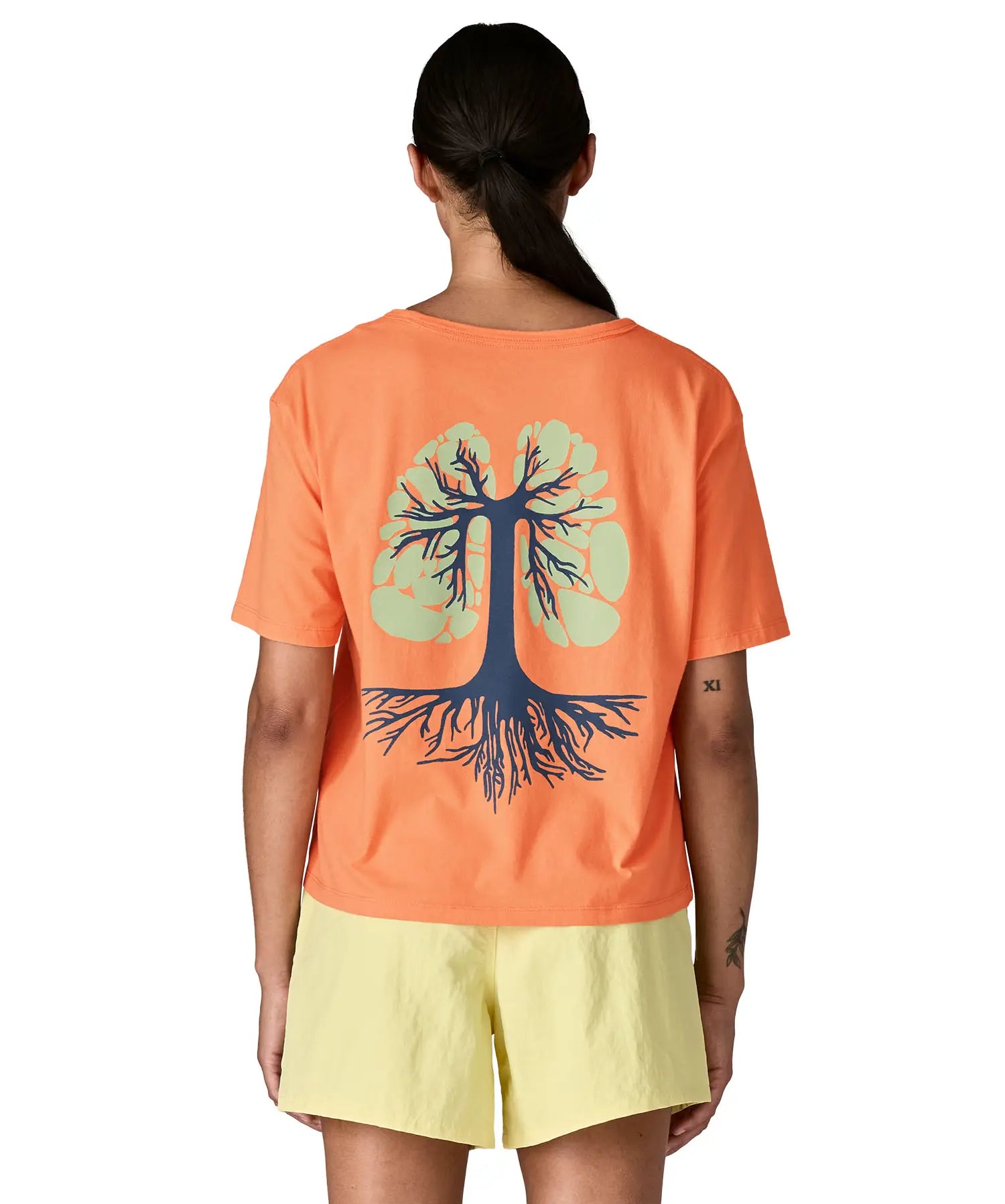 Woman wearing Patagonia's women's easy cut short sleeve t-shirt in bright orange with blue tree roots graphic on the back