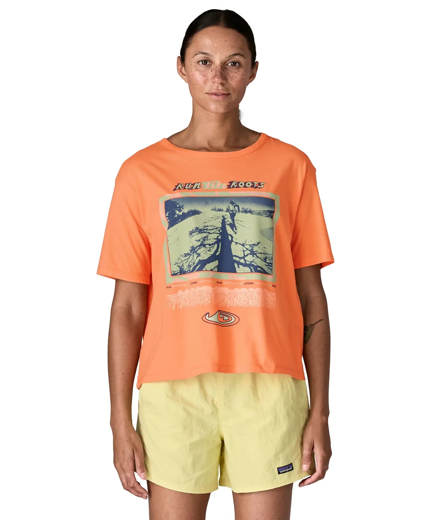 Woman wearing Patagonia's women's easy cut short sleeve t-shirt in bright orange with retro run like roots graphic on the front