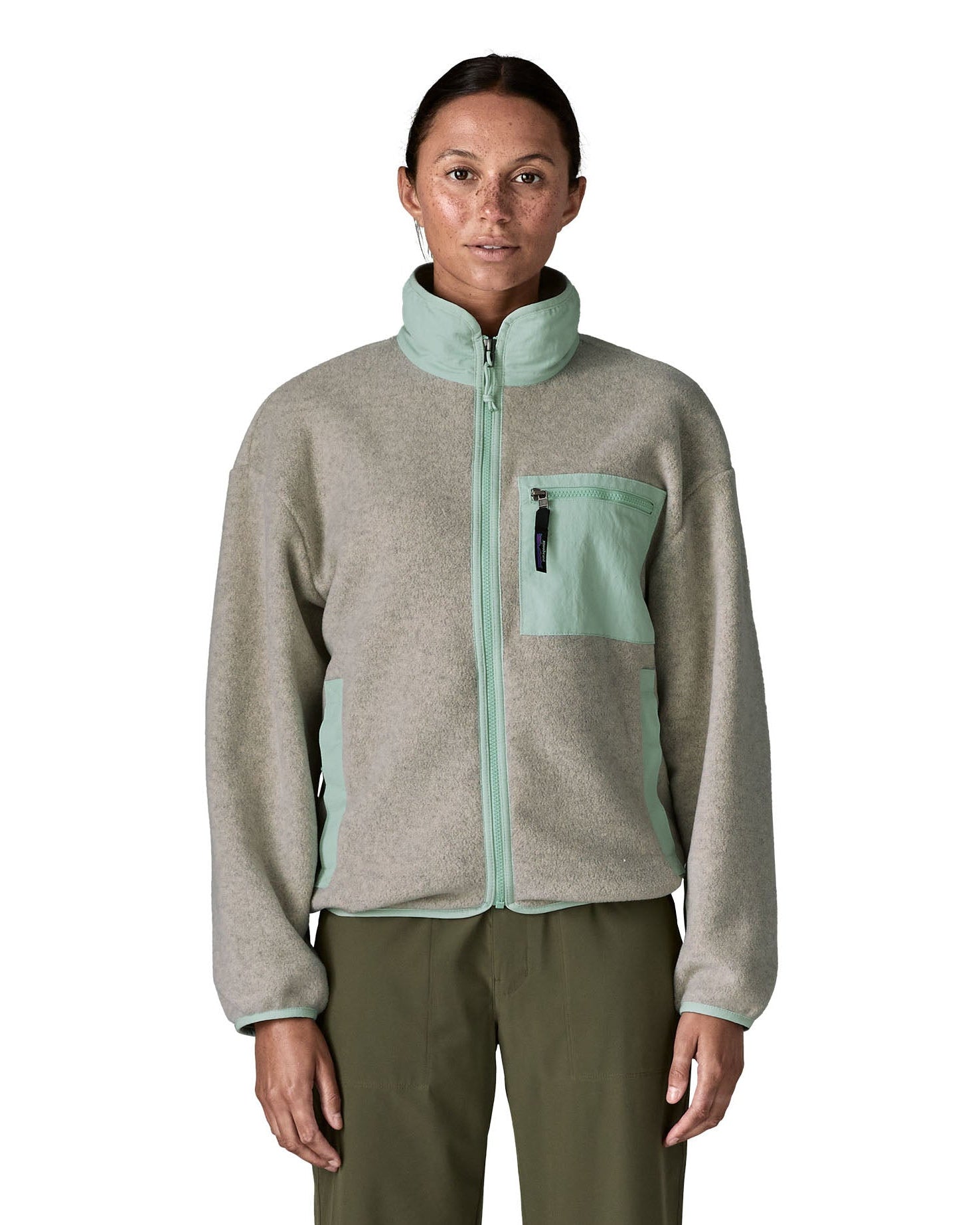 Woman wearing Patagonia's women's synchilla fleece jacket in light grey and blue trim. With the front zip fully fastened 