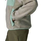 Side of a woman wearing Patagonia's women's synchilla fleece jacket in light grey. Jacket has relaxed fit and sits at the hips