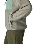 Side of a woman wearing Patagonia's women's synchilla fleece jacket in light grey. Jacket has relaxed fit and sits at the hips