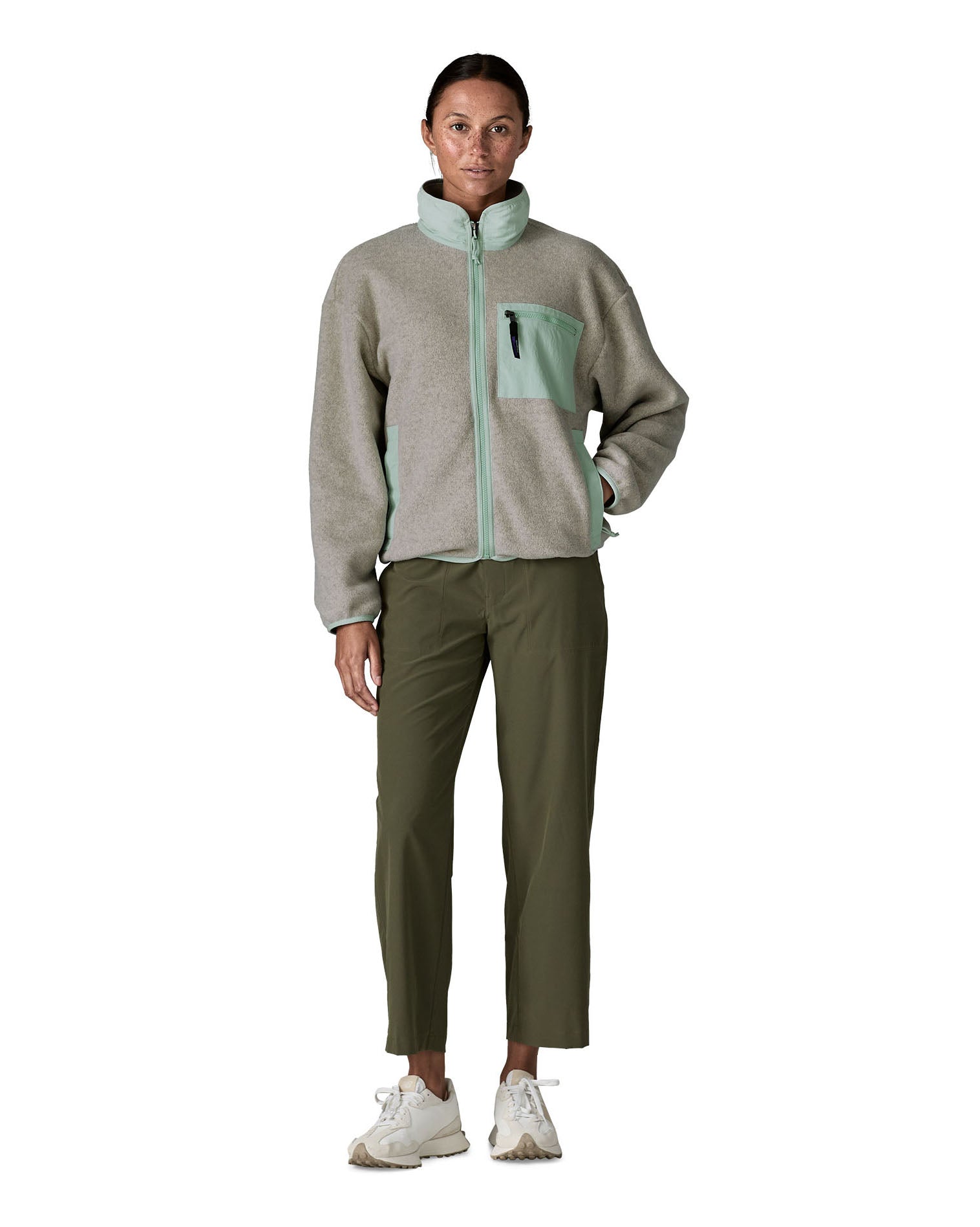 Woman wearing Patagonia women's synchilla fleece jacket in light grey and blue trim. Jacket has relaxed fit and sits at the hips
