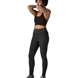 A female standing in front of a white background wearing a black sports vest and the Patagonia women's sports leggings in black with side pockets.