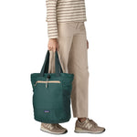 A close up of the Patagonia Terravia tote bag in cascade green carried by an adult by the handles showing the front zip details and 2 side pockets.