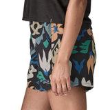 Side of woman wearing Patagonia quick drying women's baggies shorts in black with repeating abstract design. Shorts have loose fit