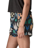 Side of woman wearing Patagonia quick drying women's baggies shorts in black with repeating abstract design. Shorts have loose fit