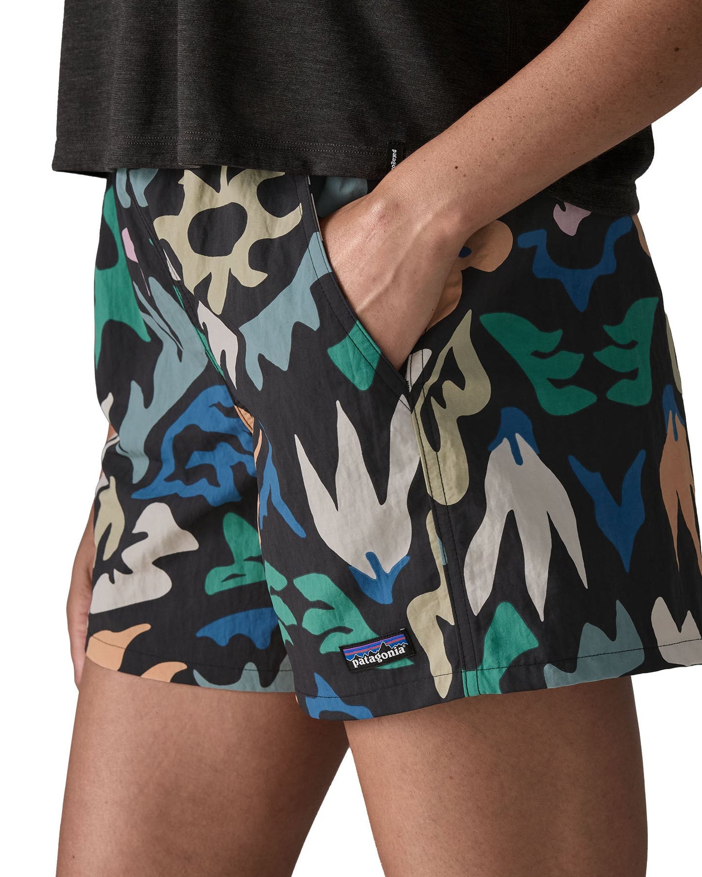 Side of woman wearing Patagonia quick drying women's baggies shorts in black with repeating abstract design with hand in side pocket