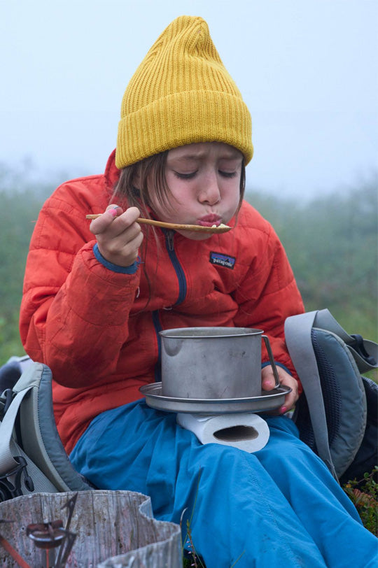 Child in Patagonia red jacket and yellow beanie eating from a bowl outdoors