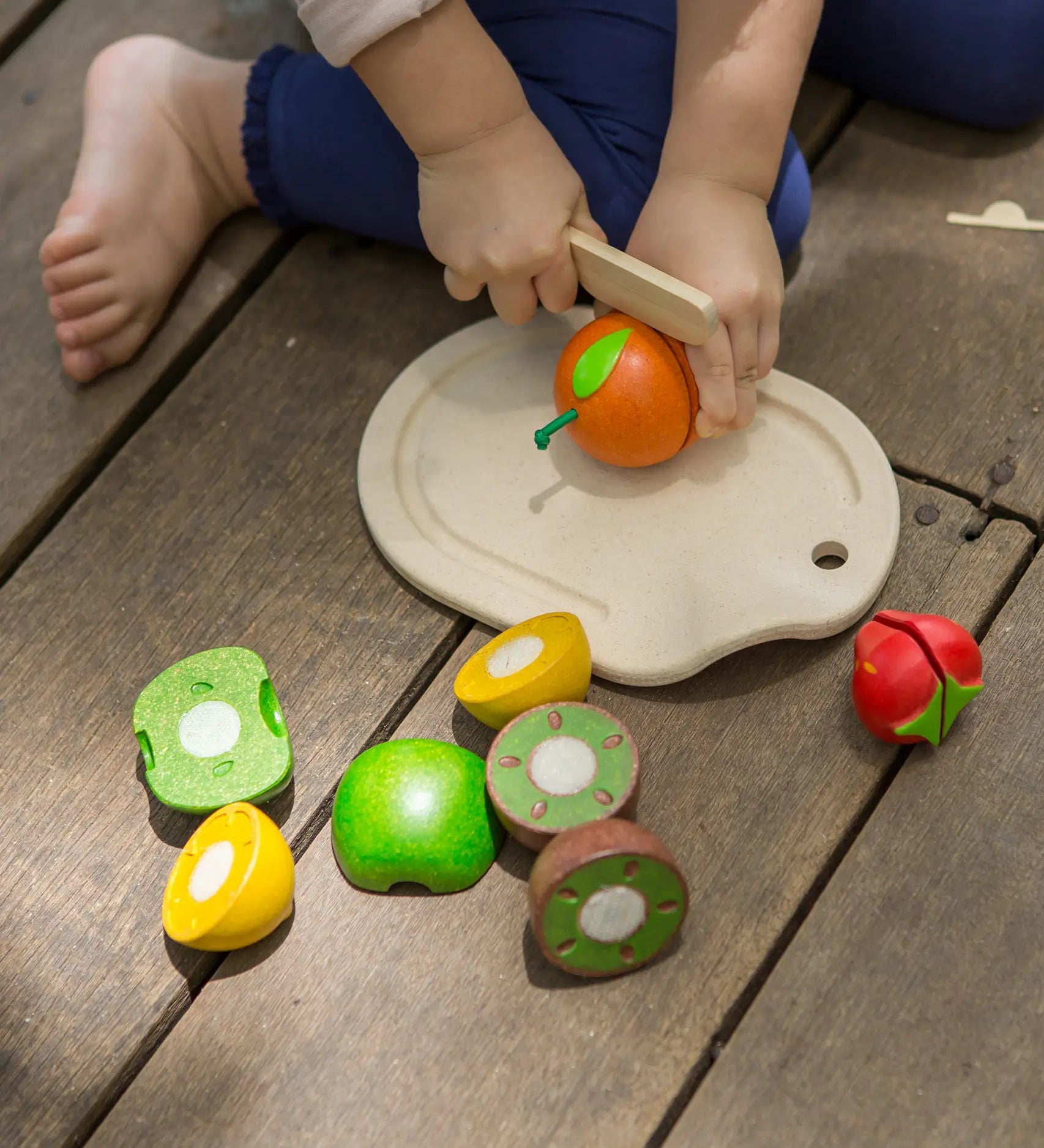 Child holding a wooden knife against a orange on a serving tray from the PlanToys assorted fruit set