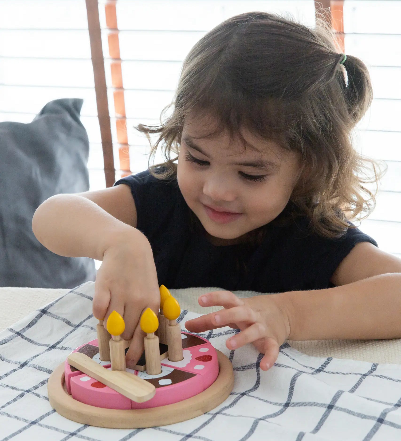 Child playing with the PlanToys wooden birthday cake set with wooden candles inside the holes