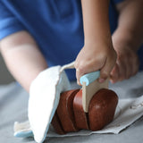 Child using the wooden cutter on a pretend bread loaf from the PlanToys bread loaf play set
