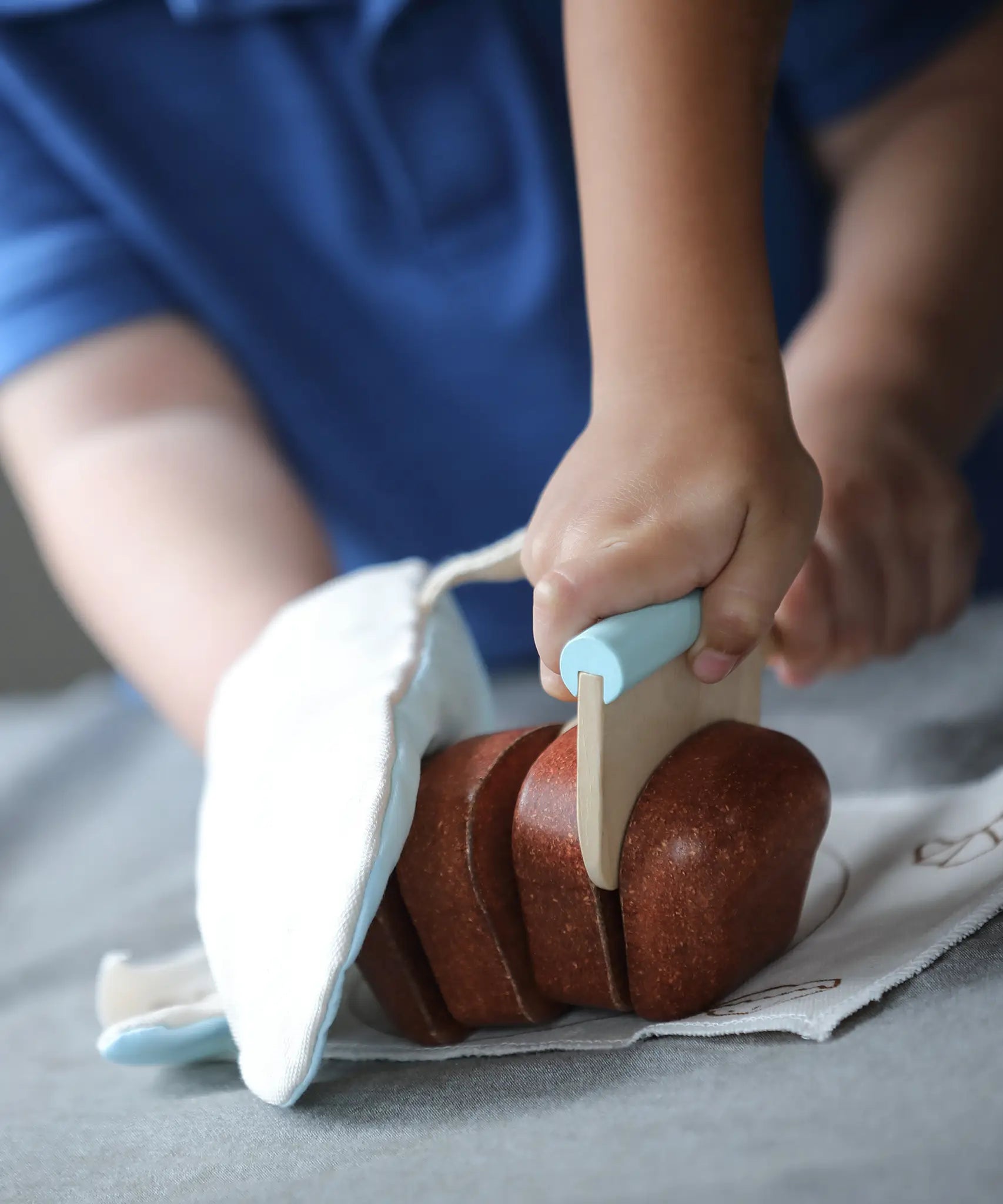 Child using the wooden cutter on a pretend bread loaf from the PlanToys bread loaf play set