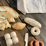 Loose play food pieces next to the cotton bag from the PlanToys bread play set