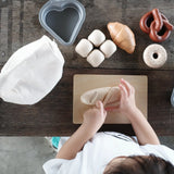 Overhead view of a child holding the wooden knife on a pretend bread roll from the PlanToys bread play set on a table