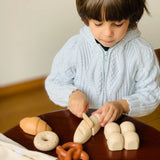 Child holding the wooden knife on a pretend bread roll from the PlanToys bread play set