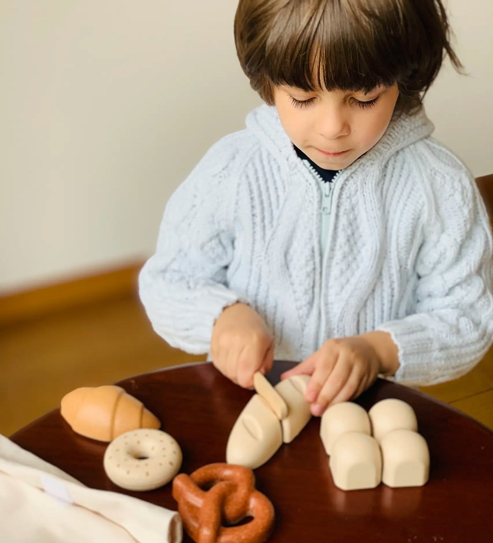 Child holding the wooden knife on a pretend bread roll from the PlanToys bread play set
